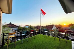 A balcony with a flag, chairs, and a view of houses during sunset. - Sekar Tunjung Guest House Seminyak Bali (Denpasar)