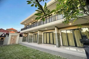 A modern two-story house with a balcony, large windows, and a well-maintained lawn.