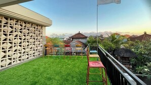 A balcony with a flag, a white lattice fence, and a view of houses and greenery. - Sekar Tunjung Guest House Seminyak Bali (Denpasar)