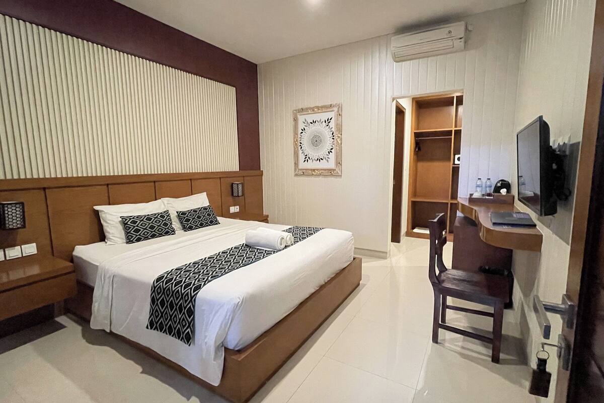 Une chambre d’hôtel avec un grand lit, un bureau avec une chaise, une télévision et une armoire.