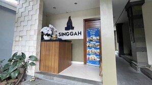 A reception area with a wooden desk, a sign reading "SINGGAH," and a menu board. - Singgah Hotel Seminyak (Seminyak)