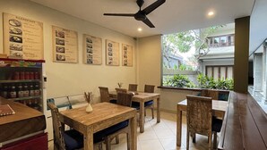A restaurant with wooden tables and chairs, a ceiling fan, and menu boards on the wall. - Singgah Hotel Seminyak (Seminyak)