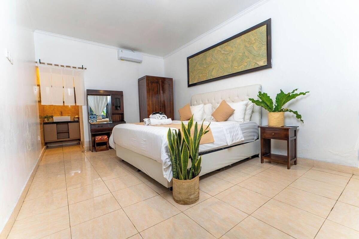 A bedroom with a bed, a bedside table with a plant, a wardrobe, and a painting on the wall.