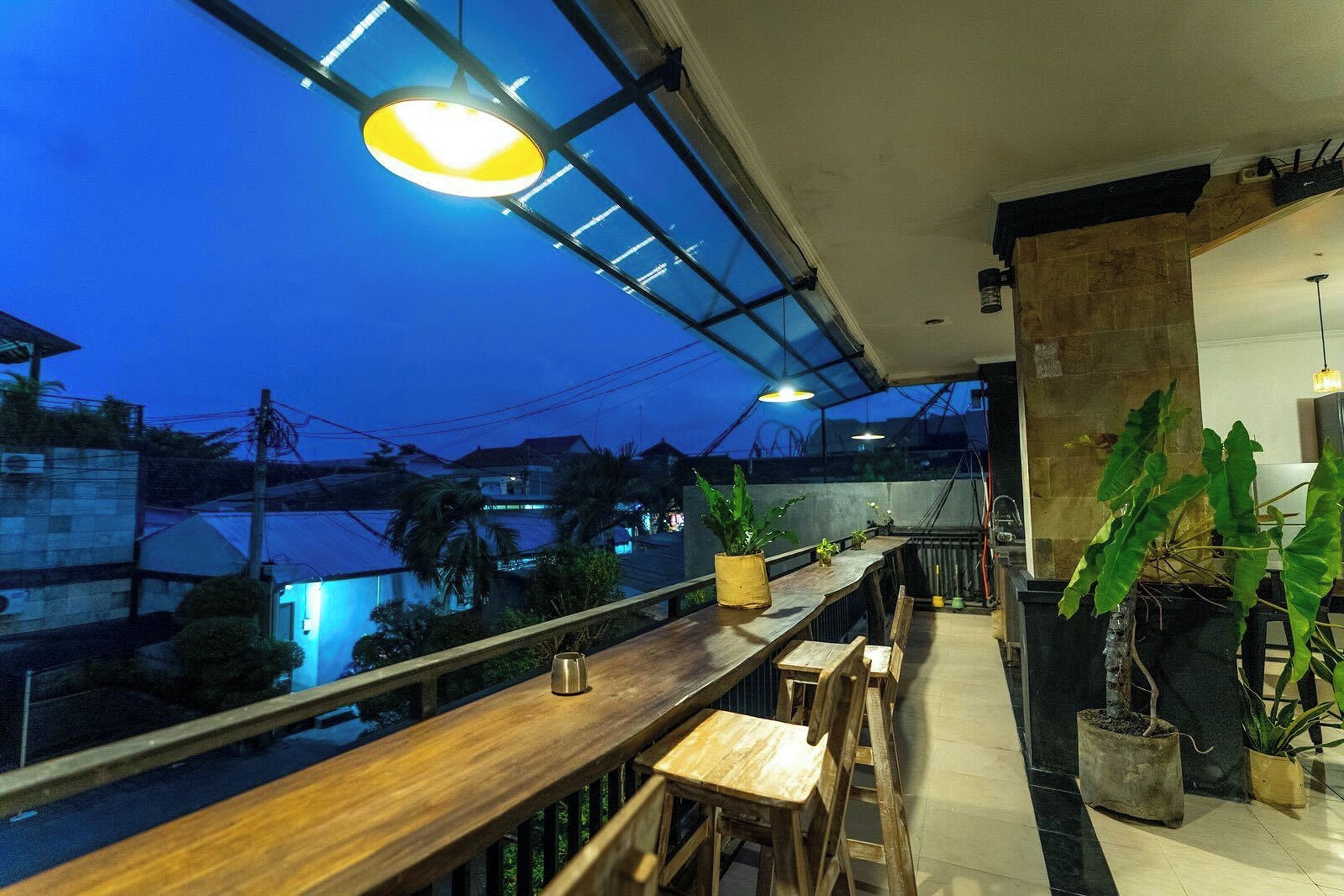 A rooftop bar with wooden seating, potted plants, and a view of the cityscape at dusk.