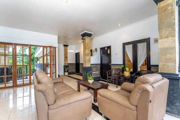 A spacious lobby with beige sofas, a wooden coffee table, and a stone pillar. - Tendan Residence (Denpasar)