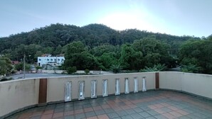 Una terraza en la azotea con vistas a una colina boscosa, un edificio blanco y un suelo de baldosas.