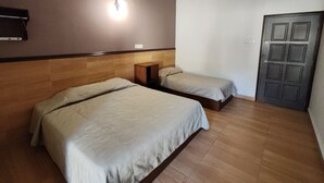 Habitación de hotel con dos camas, cabecera de madera, mesita de noche, lámpara de pared y una puerta.
