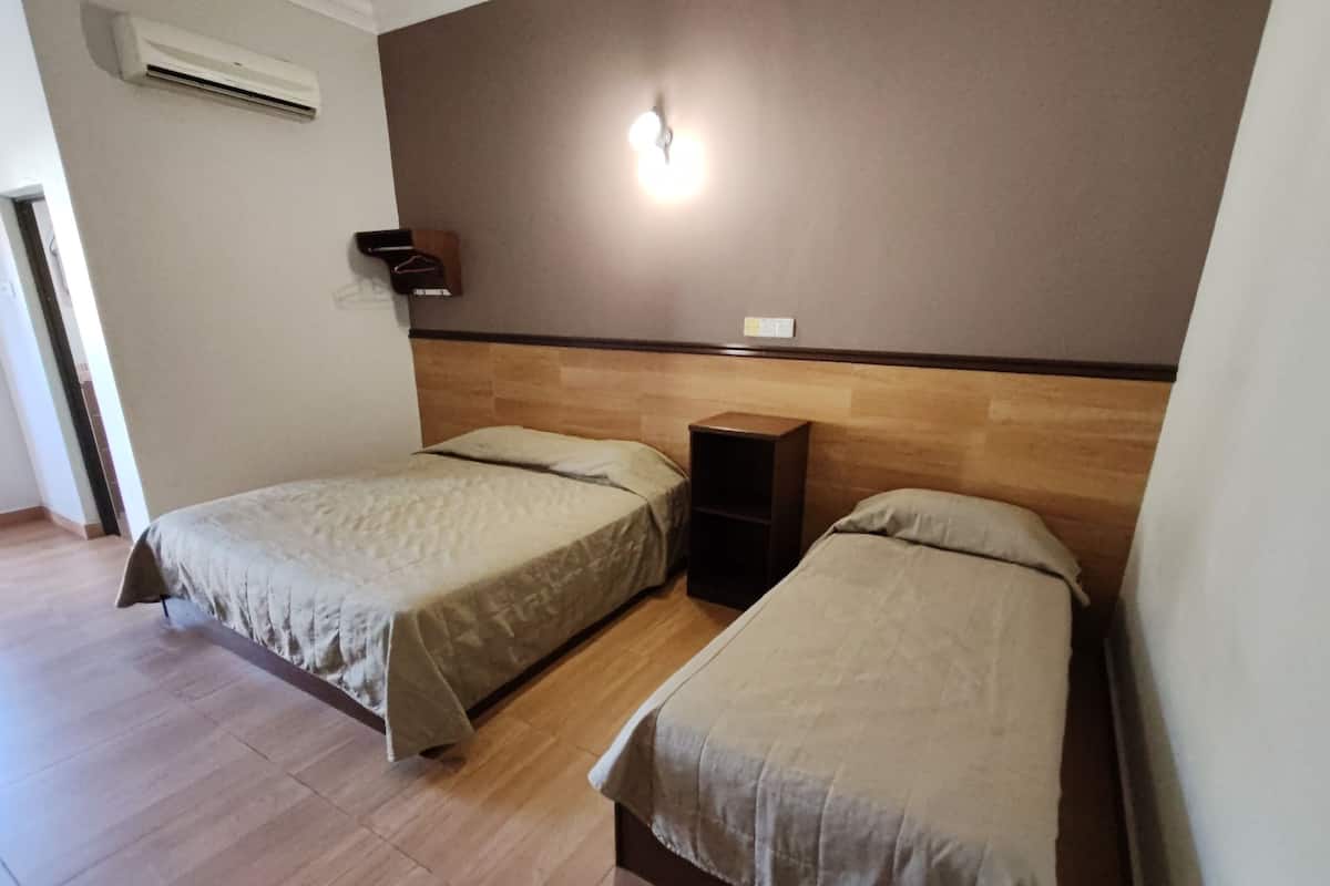 Une chambre avec deux lits simples, une tête de lit en bois, une étagère fixée au mur et un appareil de climatisation.