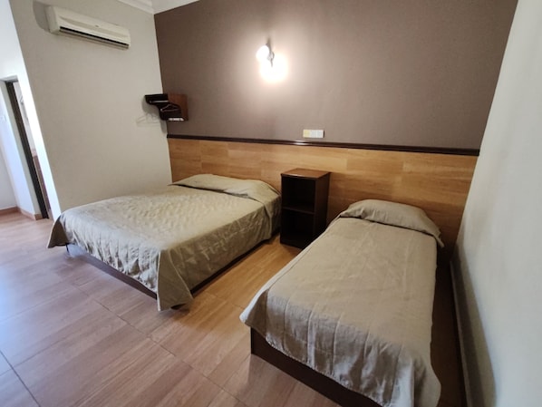 A room with two single beds, a wooden headboard, a wall-mounted shelf, and an air conditioning unit.