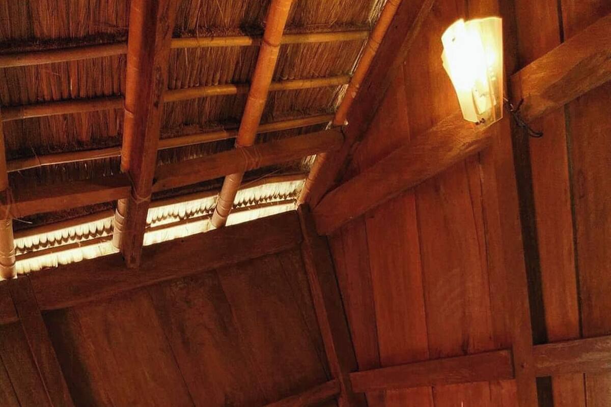 A wooden cabin room with a bed, a thatched roof, and a wall-mounted light fixture.
