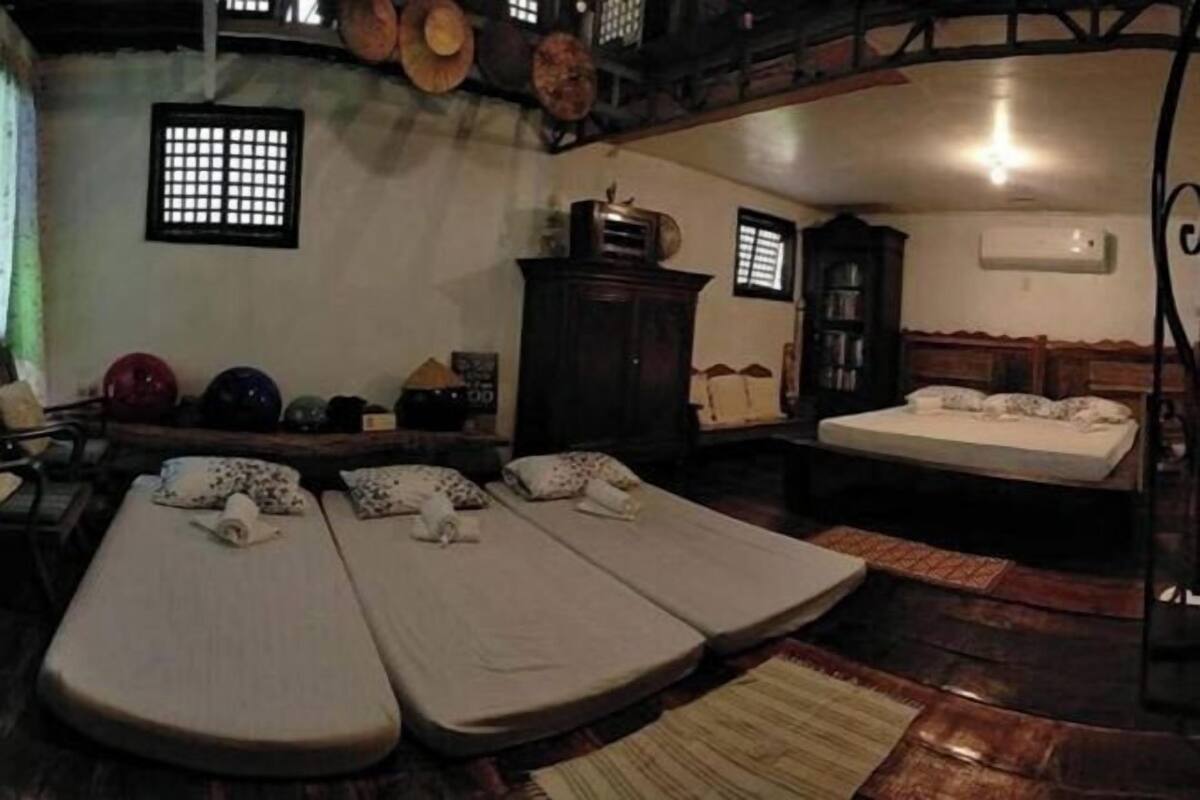 A room with two single beds, a wooden cabinet, a small table, and a window with a grid pattern.