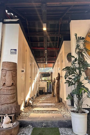 A hallway with a stone face sculpture, a restroom sign, and a potted plant. - Surfer'S Villa (San Juan)