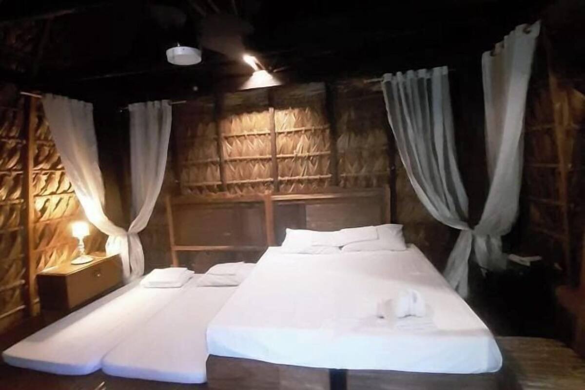 A single bed with white linens, a bedside table with a lamp, and a curtain-covered window.