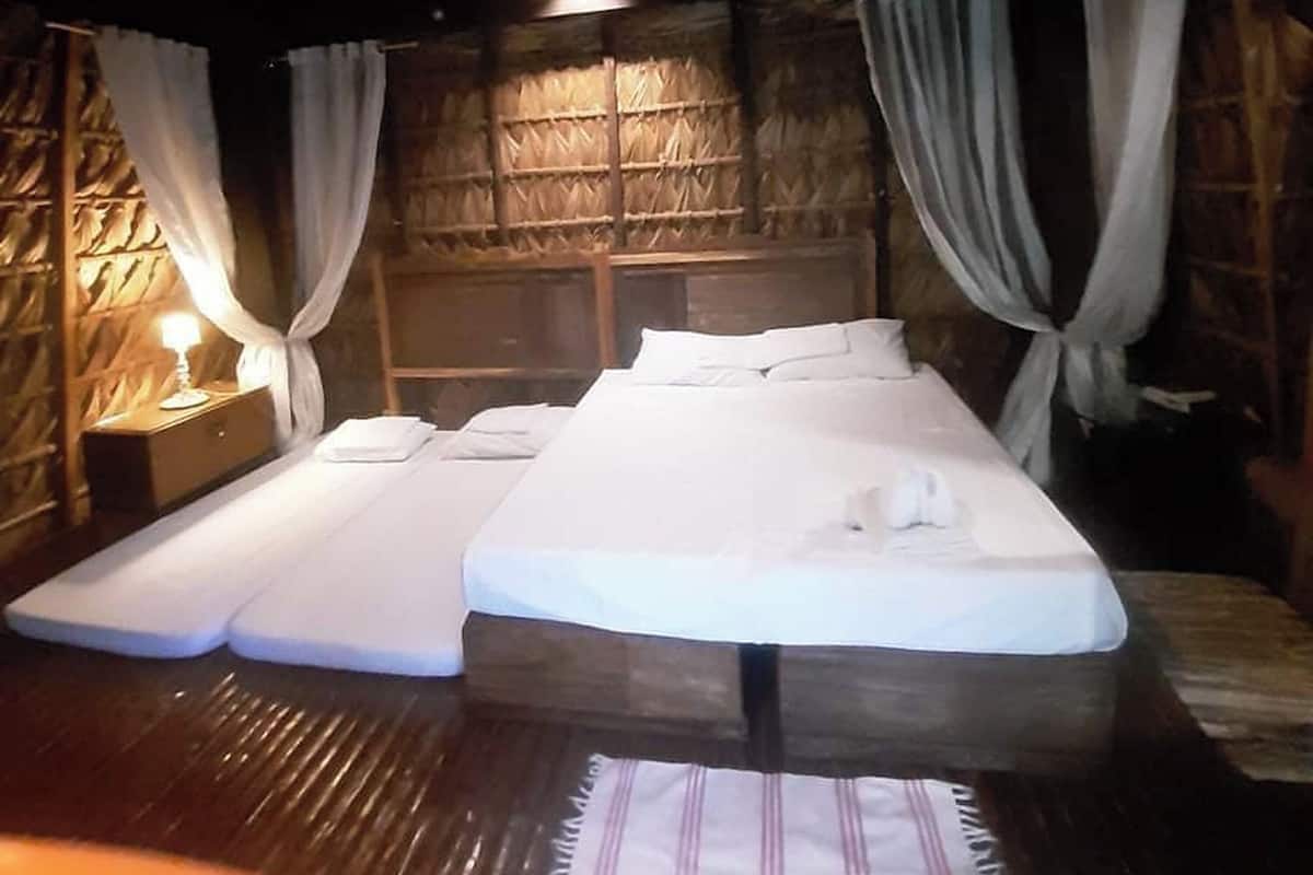 A room with two beds, a wooden ceiling, and a thatched wall.