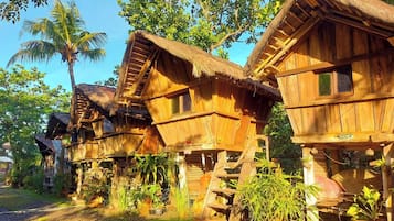 Accommodations feature elevated, thatched-roof structures amidst lush greenery and palm trees.
