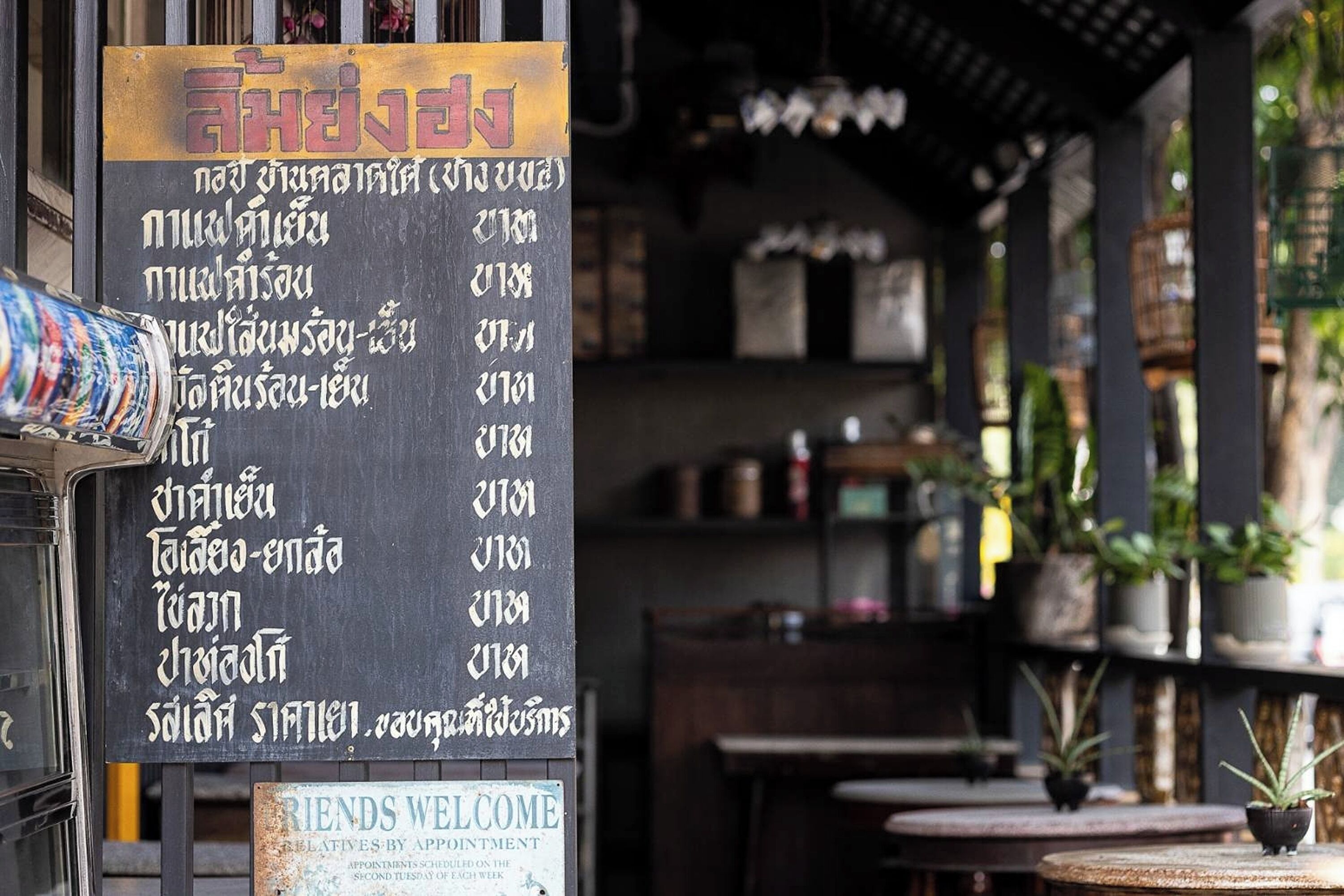 Een restaurant met een menubord waarop verschillende gerechten en prijzen in Thaise letters staan.
