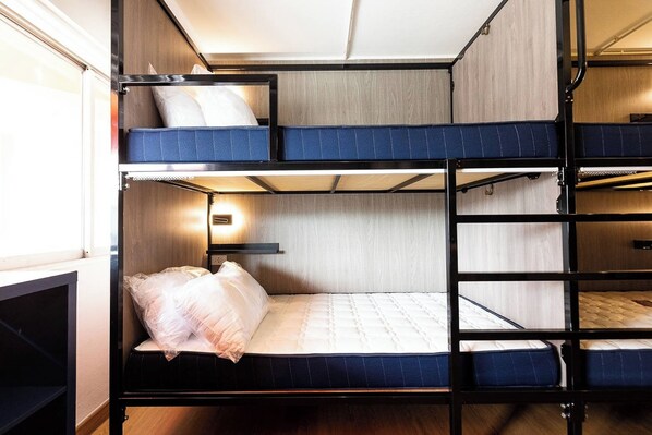 A bunk bed room with a wooden headboard, a bedside table, and a wall-mounted light. - Orange Lodge (Bangkok)