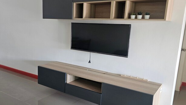 Un salon moderne doté d’un téléviseur à écran plat fixé au mur, d’étagères en bois et d’un meuble de rangement intégré avec des tiroirs.