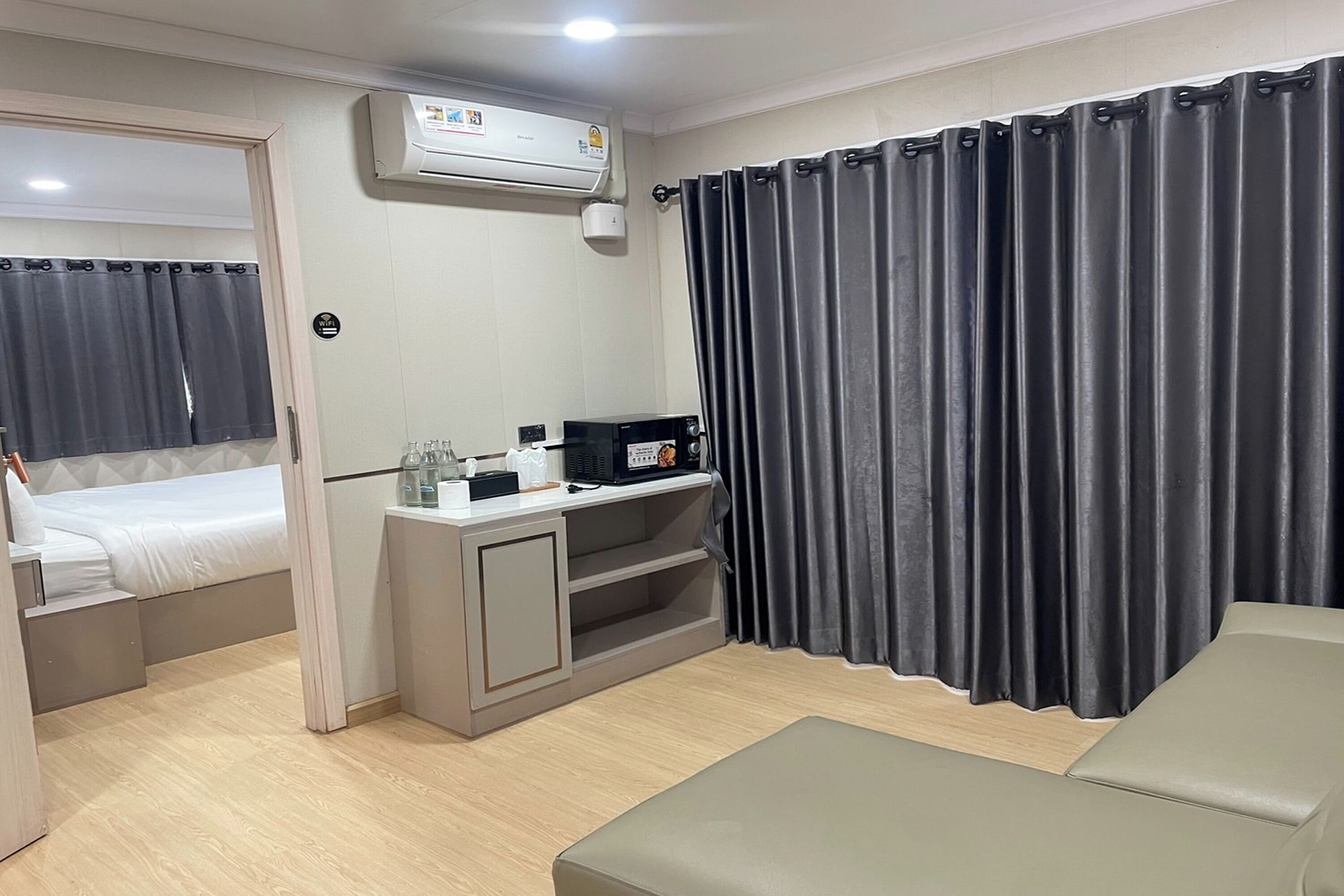 Una habitación de hotel compacta con cama, un escritorio pequeño con computadora, un sofá y un ventanal con cortinas.