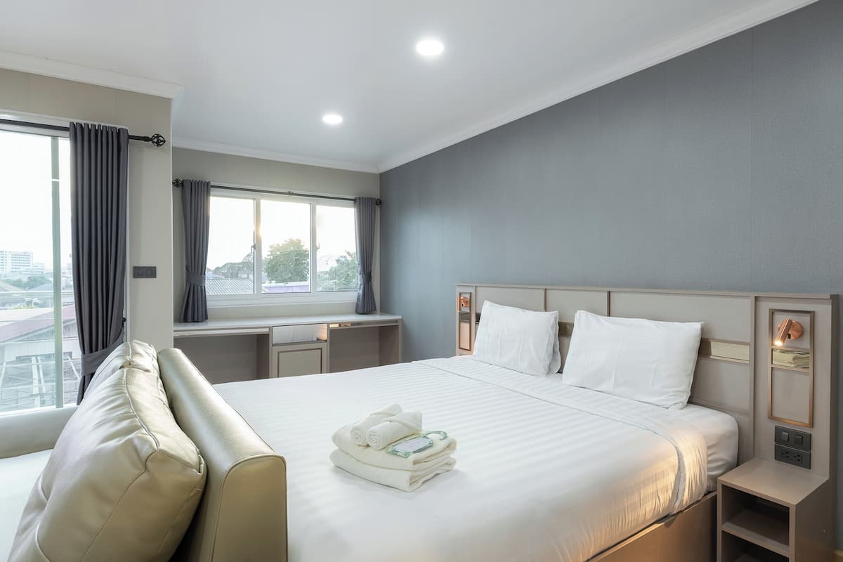 A hotel room with a large bed, a bedside table, a nightstand, a window with curtains, and a view of the city.