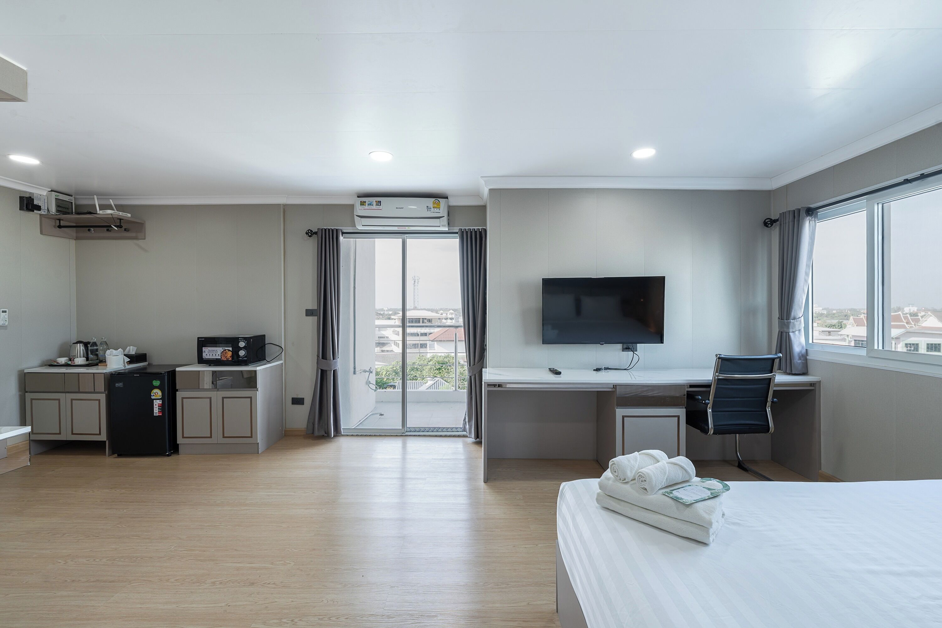 A hotel room with a bed, a desk with a TV, a kitchenette, and a balcony with a view.
