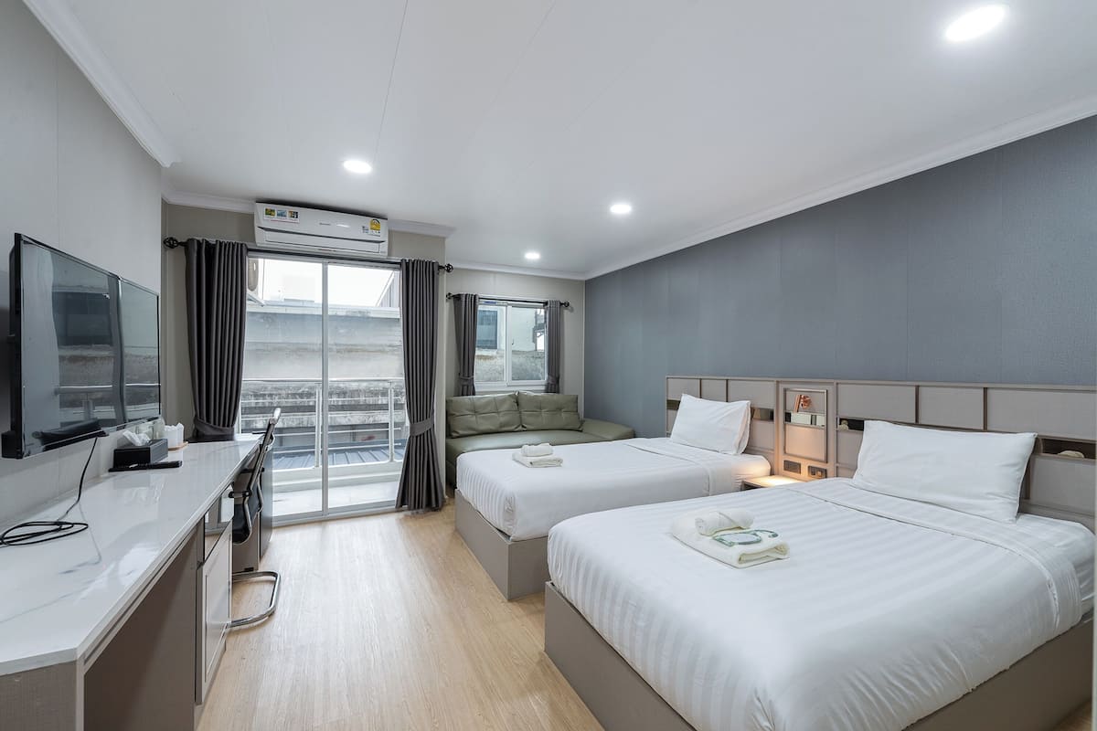 A hotel room with two beds, a desk, a television, and a balcony with curtains.
