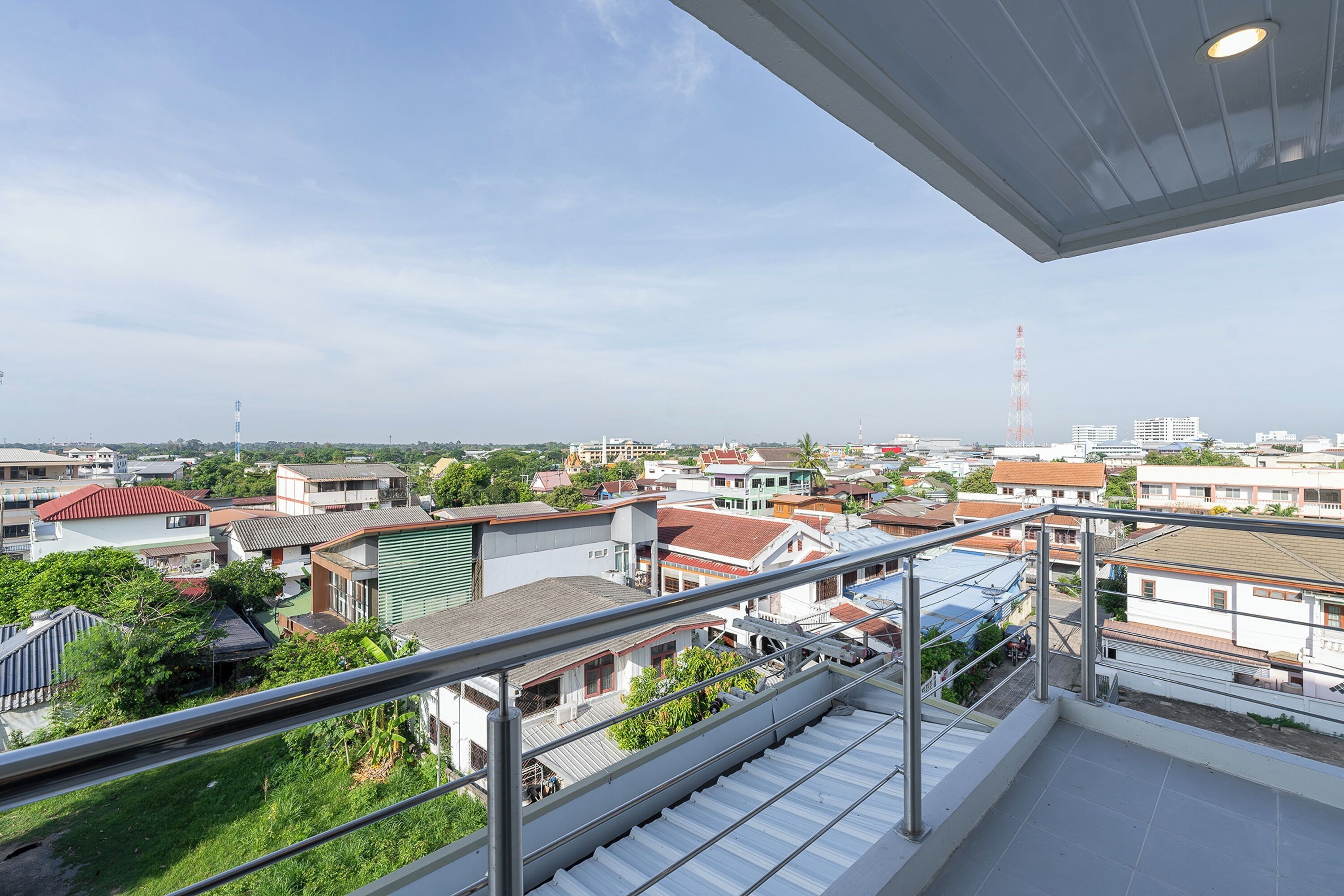 A residential area with a view from a balcony, featuring a metal railing, a staircase, and various buildings with different roof colors.