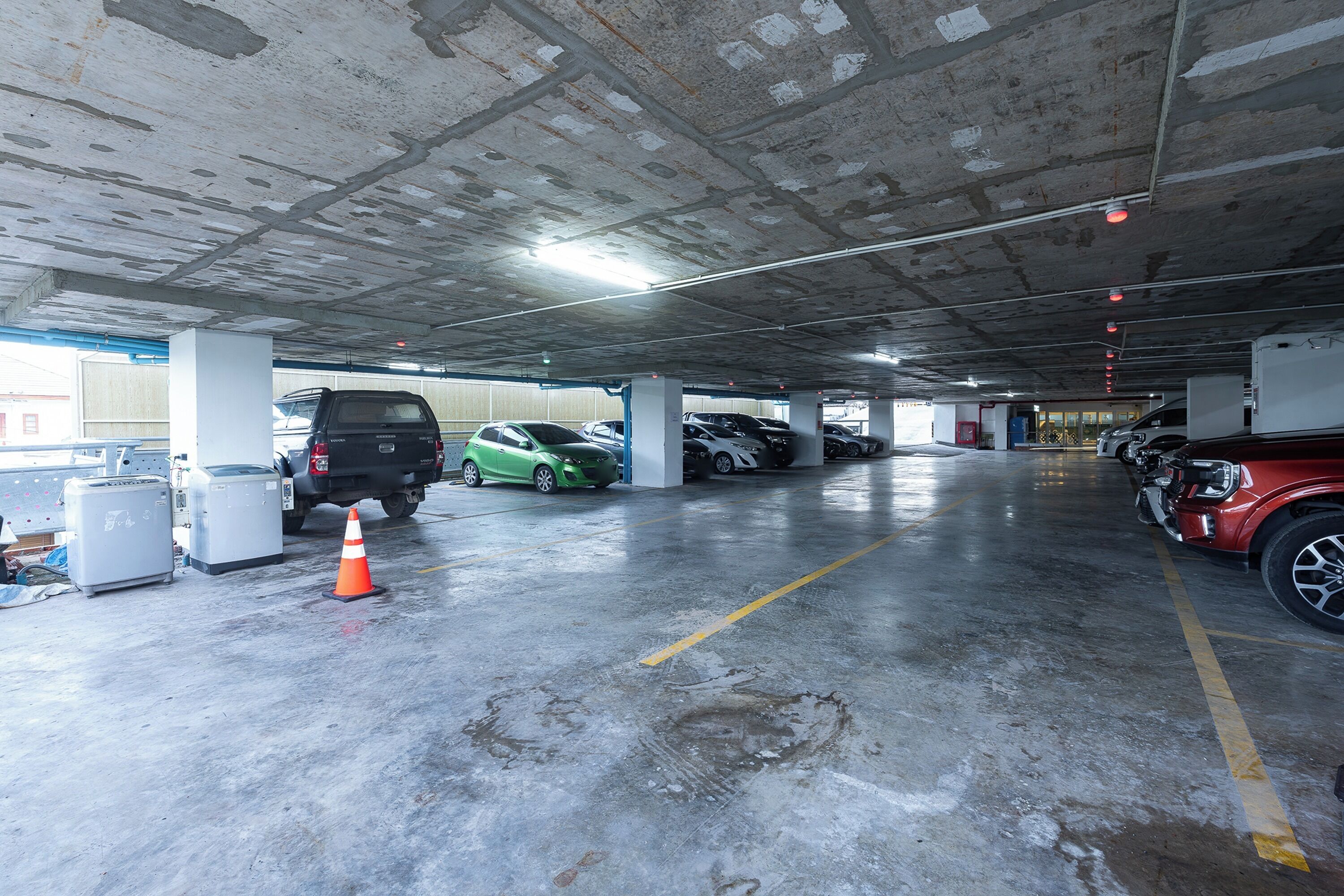 An underground parking garage with concrete pillars, marked parking spaces, and a few vehicles.