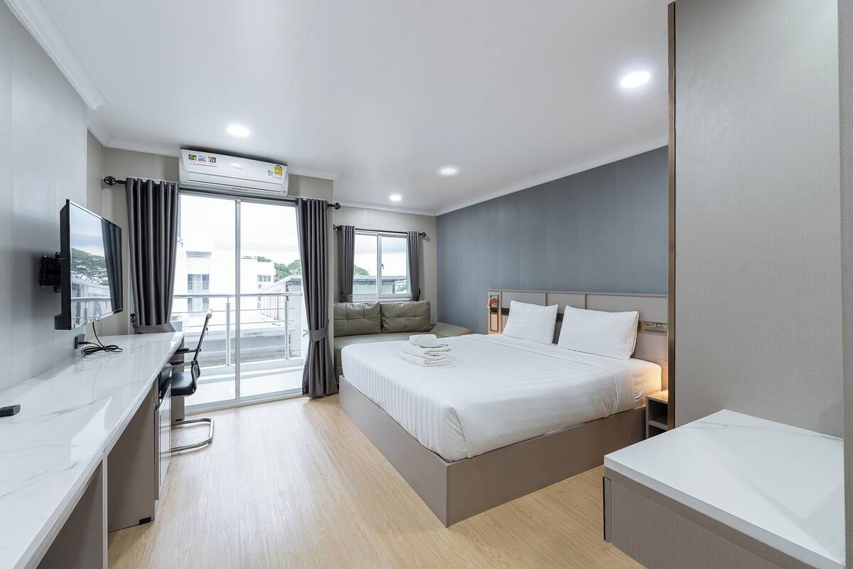 A hotel room with a bed, bedside table, TV, and a balcony with curtains.