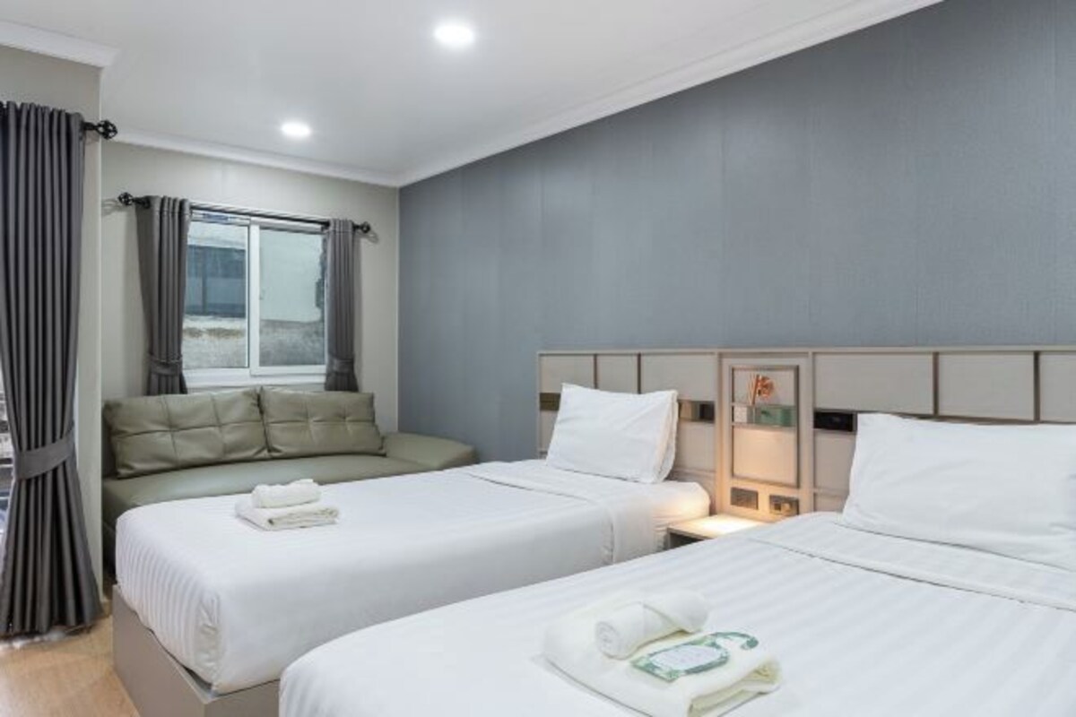 Una habitación de hotel con dos camas, un sofá, una ventana con cortinas y una mesita de noche con lámpara.