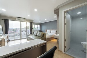 A modern hotel room with a large window, a bed, a desk, and a shower area. - Tj 4711 Residence (Maha Sarakham)