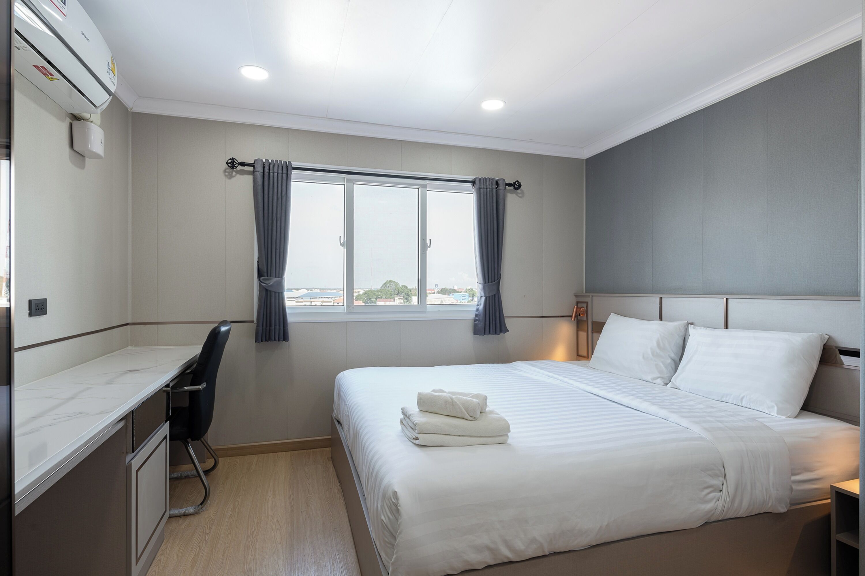A hotel room with a bed, a desk, and a window with curtains.