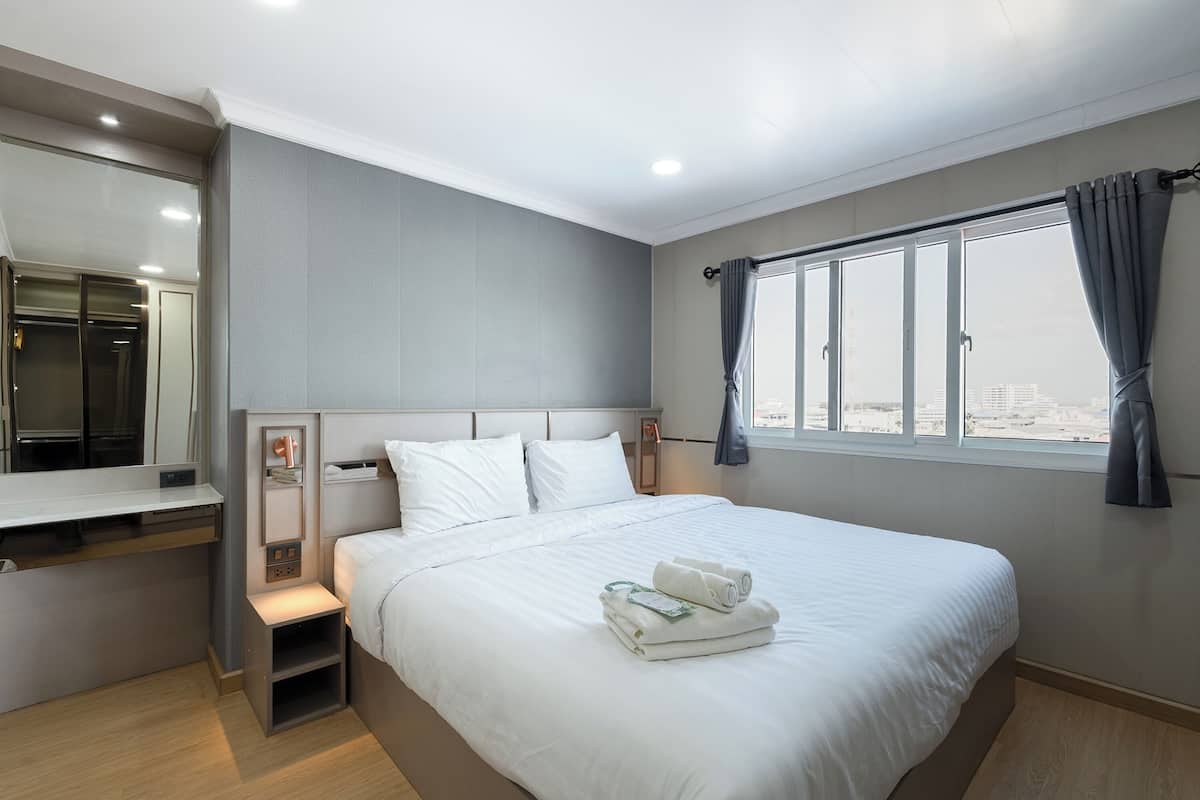 A modern hotel room with a large bed, a desk, and a window with curtains.