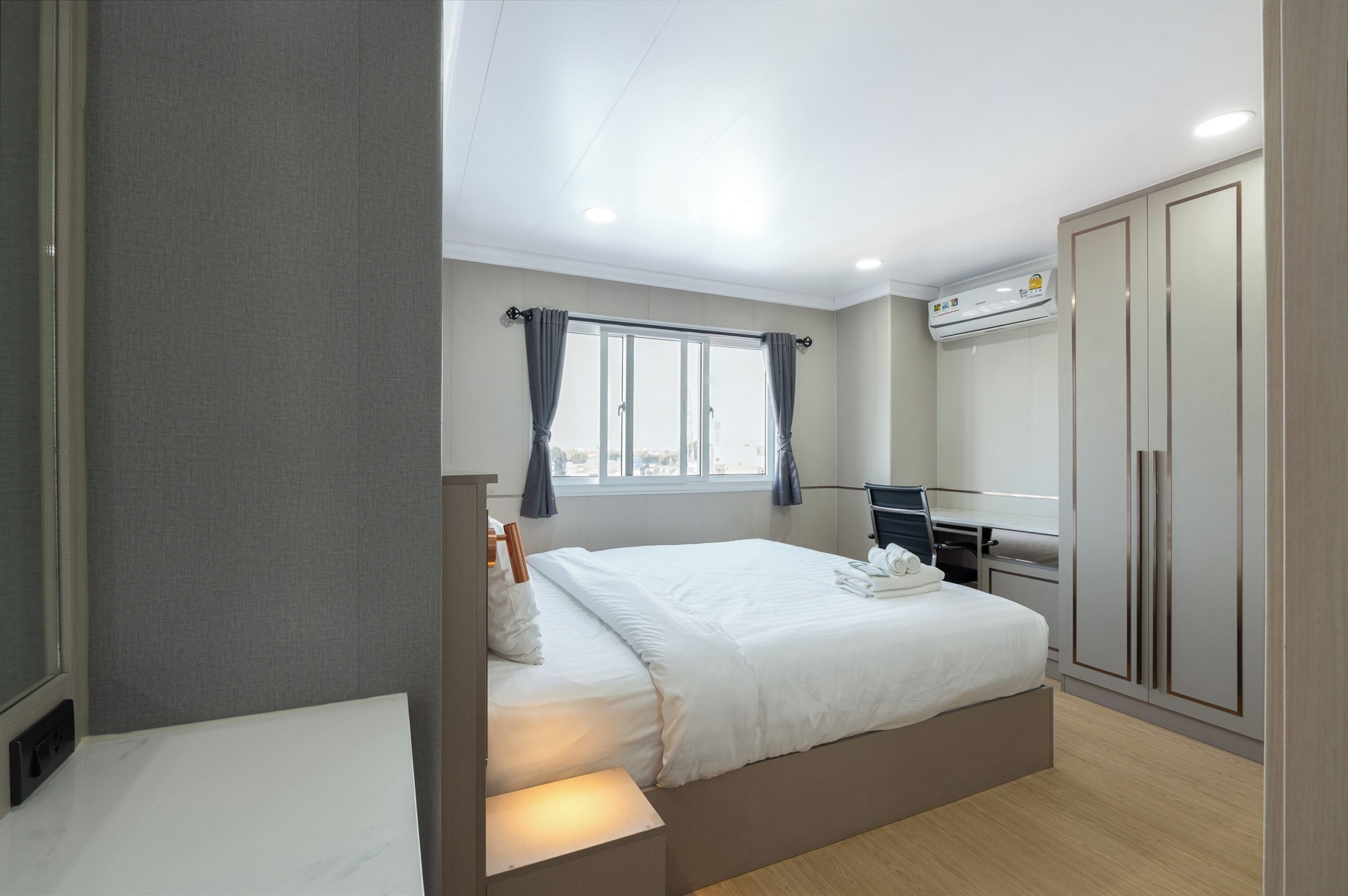 Moderni hotellihuone, jossa on suuri sänky, työpöytä ja vaatekaappi.
