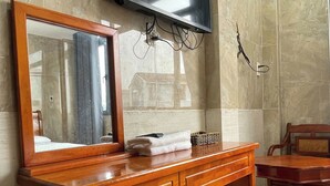 Un baño con tocador de madera, espejo, televisor de pantalla plana montado en la pared y ventilador de techo.