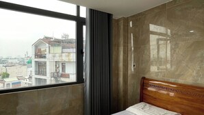 Habitación de hotel con una cama grande, cabecera de madera, vista a edificios por la ventana y una cortina.