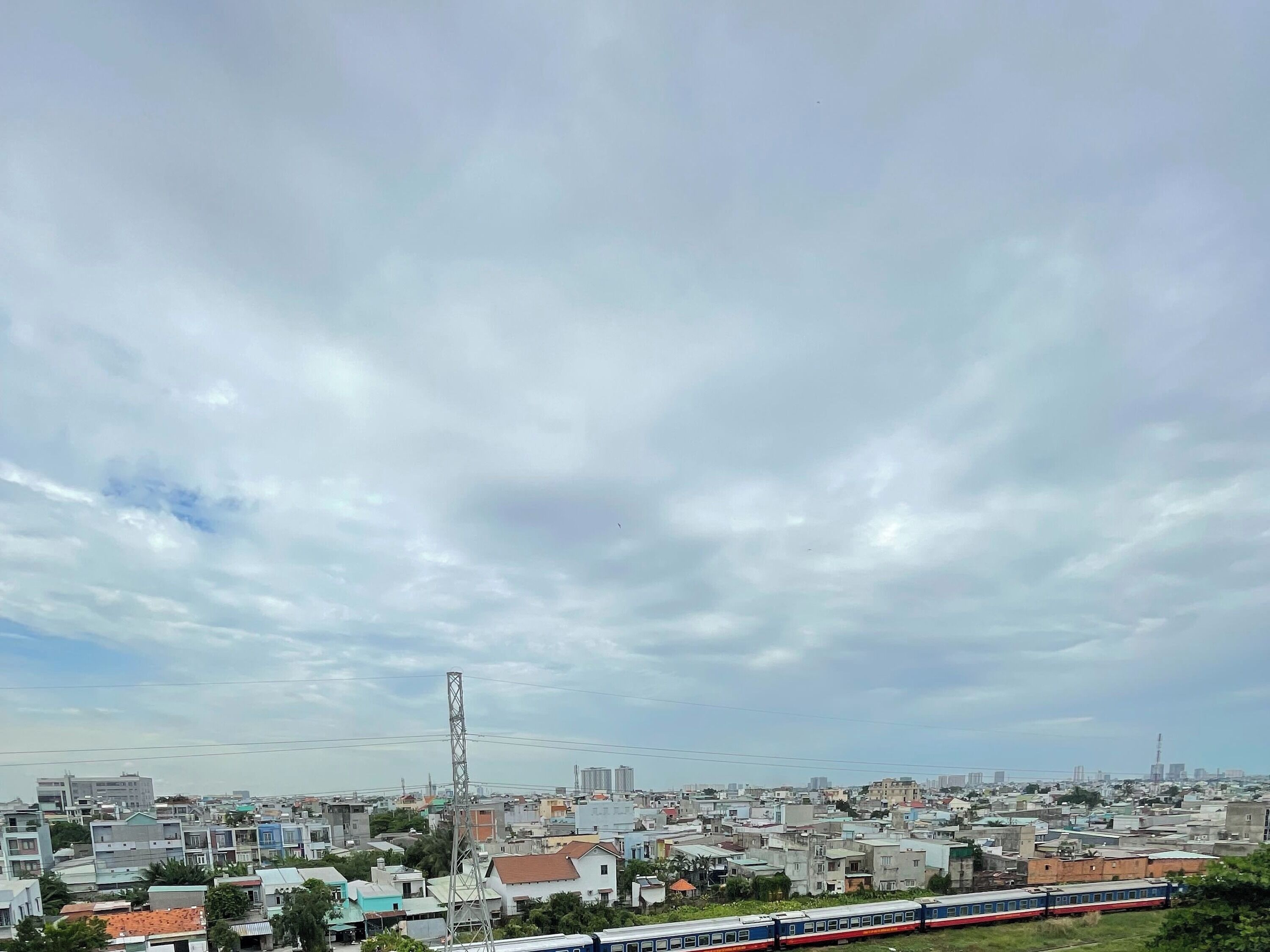 A cityscape with a train passing through, buildings, and a cloudy sky.