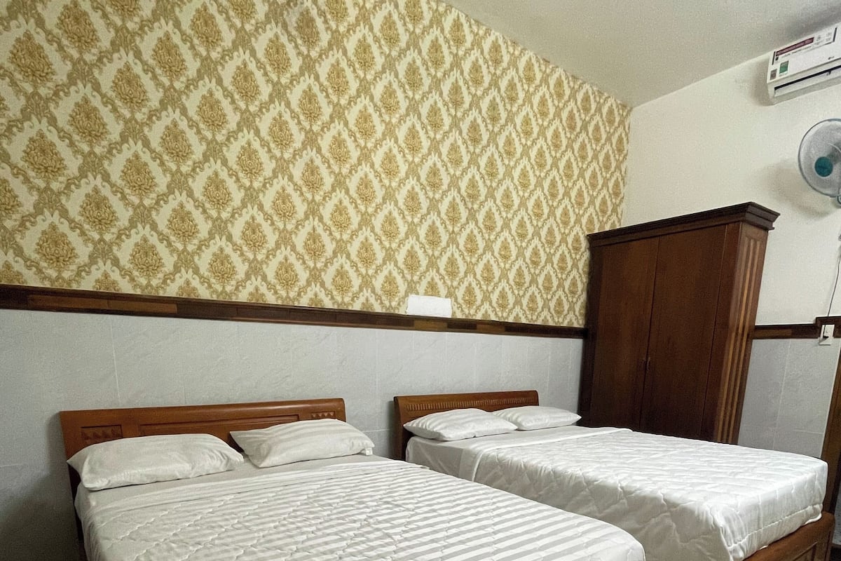Une chambre avec deux lits simples, une armoire en bois et un papier peint à motifs.