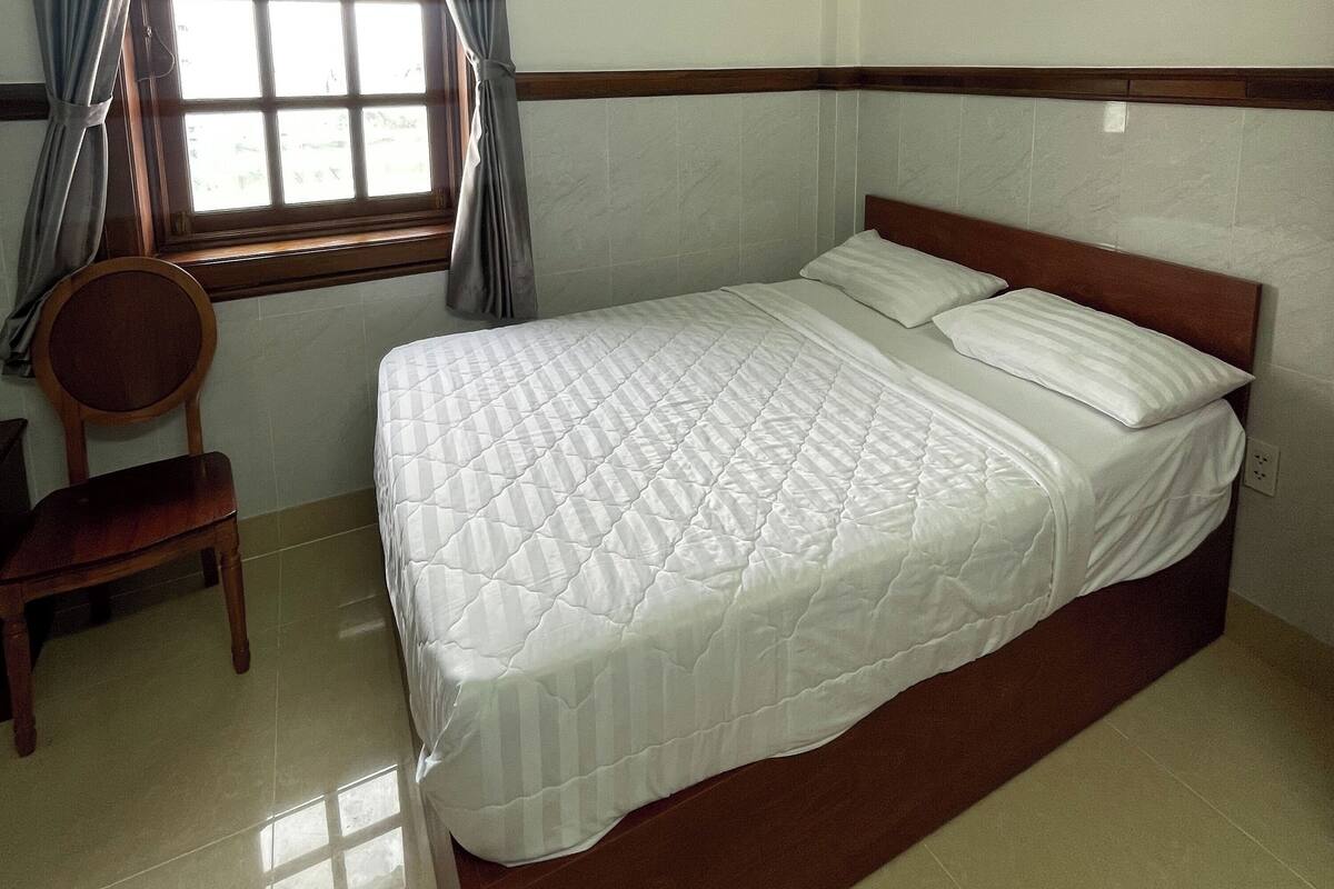 Une chambre à coucher avec un lit, une chaise, une fenêtre avec des rideaux et un plancher carrelé.