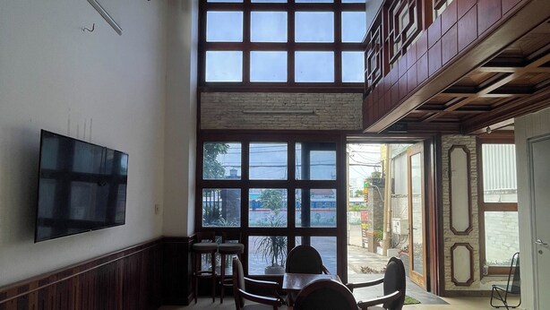 Una habitación amplia con un gran ventanal, un televisor de pantalla plana montado en la pared y una zona de comedor con sillas y una mesa.