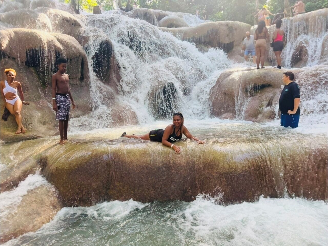 A natural water feature with multiple waterfalls and people enjoying the area.
