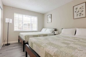 A bedroom with two beds, a standing lamp, and a window with blinds.