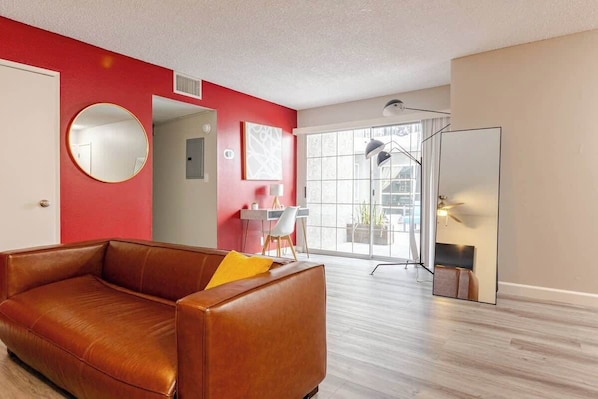 A modern living room with a brown leather sofa, a round mirror, and a large window with a view of the outside.