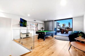 A modern living room with a pool table, a sofa, and a city view through large windows. - Luxico Wanderlust (Heated Pool) (Broadbeach Waters)