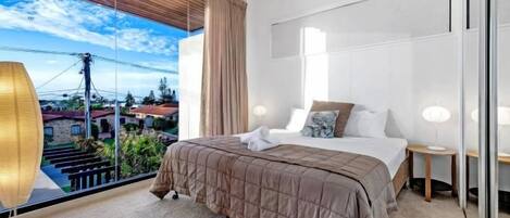 A modern bedroom with a large bed, a nightstand, a lamp, and a view of the outdoors.