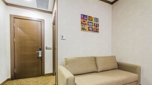 Une pièce avec une porte en bois, un canapé beige, une moquette à motifs et une œuvre d’art accrochée au mur.