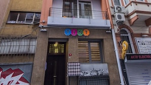 Un immeuble à plusieurs étages doté de balcons, une enseigne indiquant « TINT Residencia », et un magasin fermé avec une enseigne « AKTIF ELEKTRIK ».