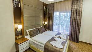 Une chambre d’hôtel avec un grand lit, une table de chevet avec une lampe, un miroir et une fenêtre avec des rideaux.