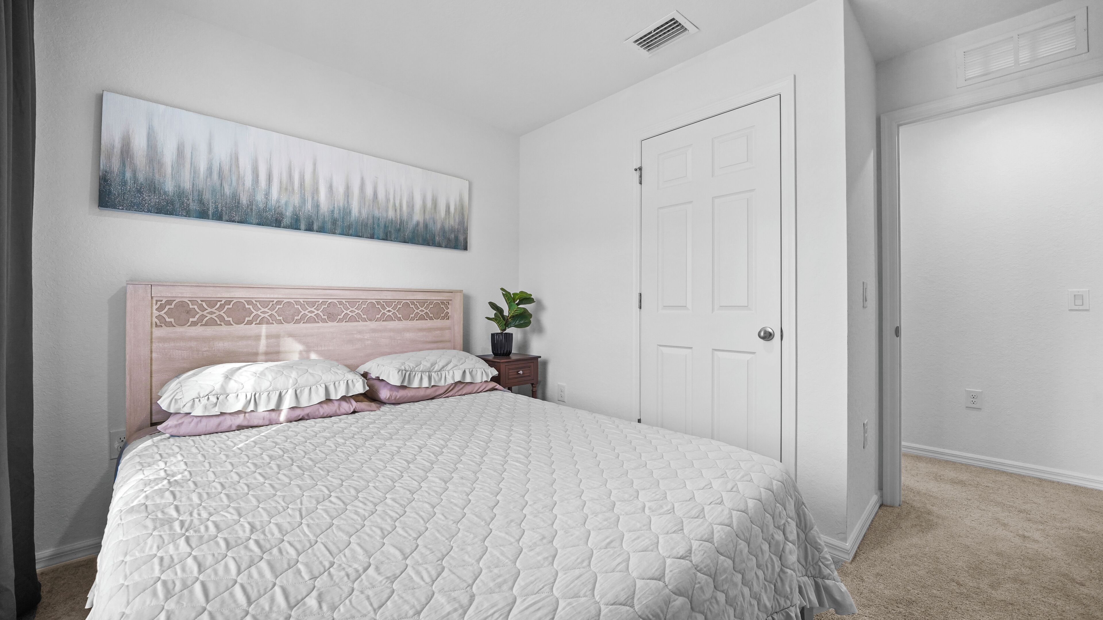 A bedroom with a large bed, a nightstand, a potted plant, and a door.