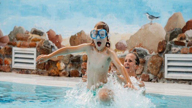 Ein Schwimmbecken mit klarem Wasser, umgeben von einer felsigen Landschaft, und ein Vogel, der auf einem Felsen sitzt.